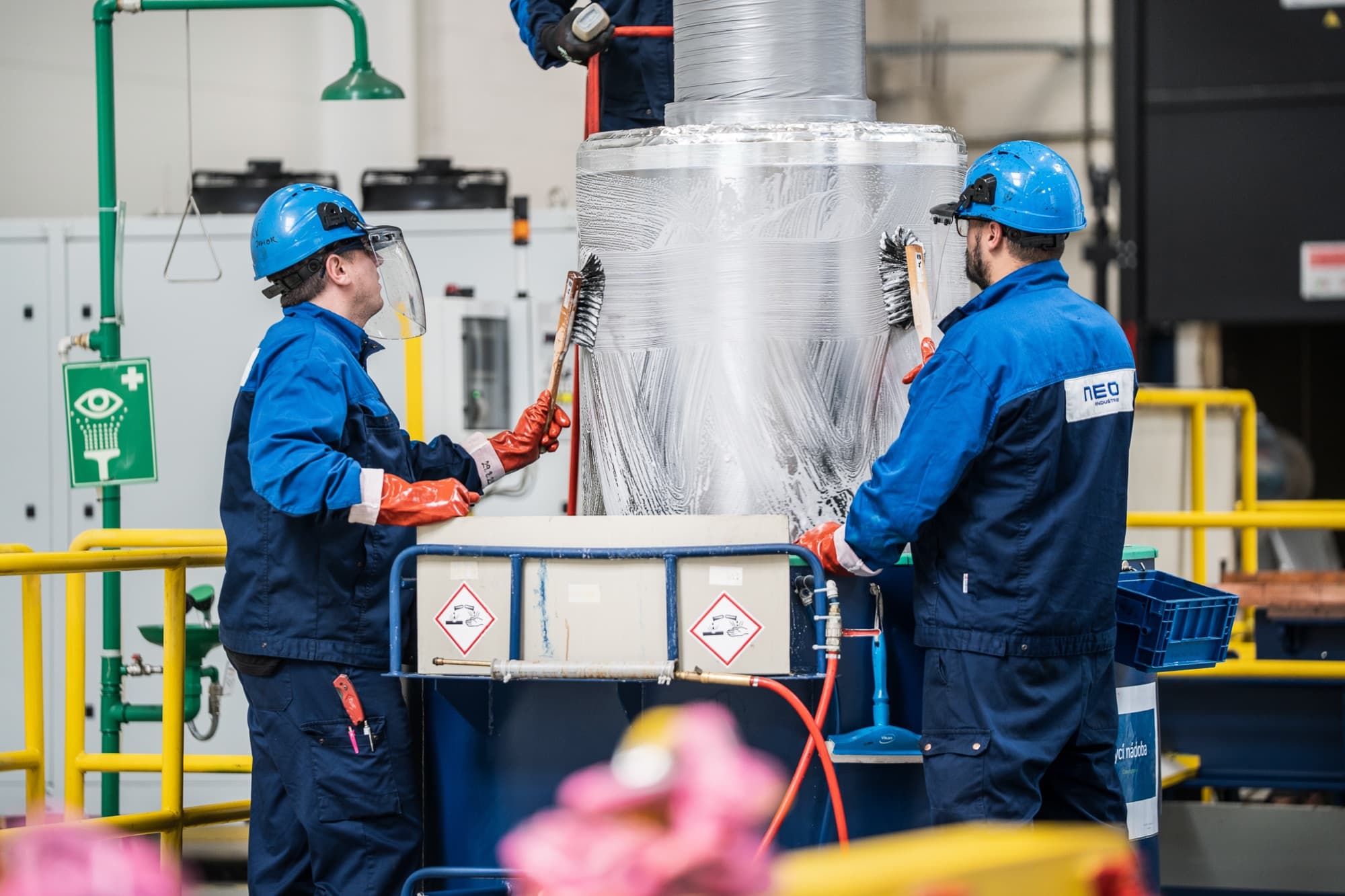 Two NEO workers in hard hats at a plating tank